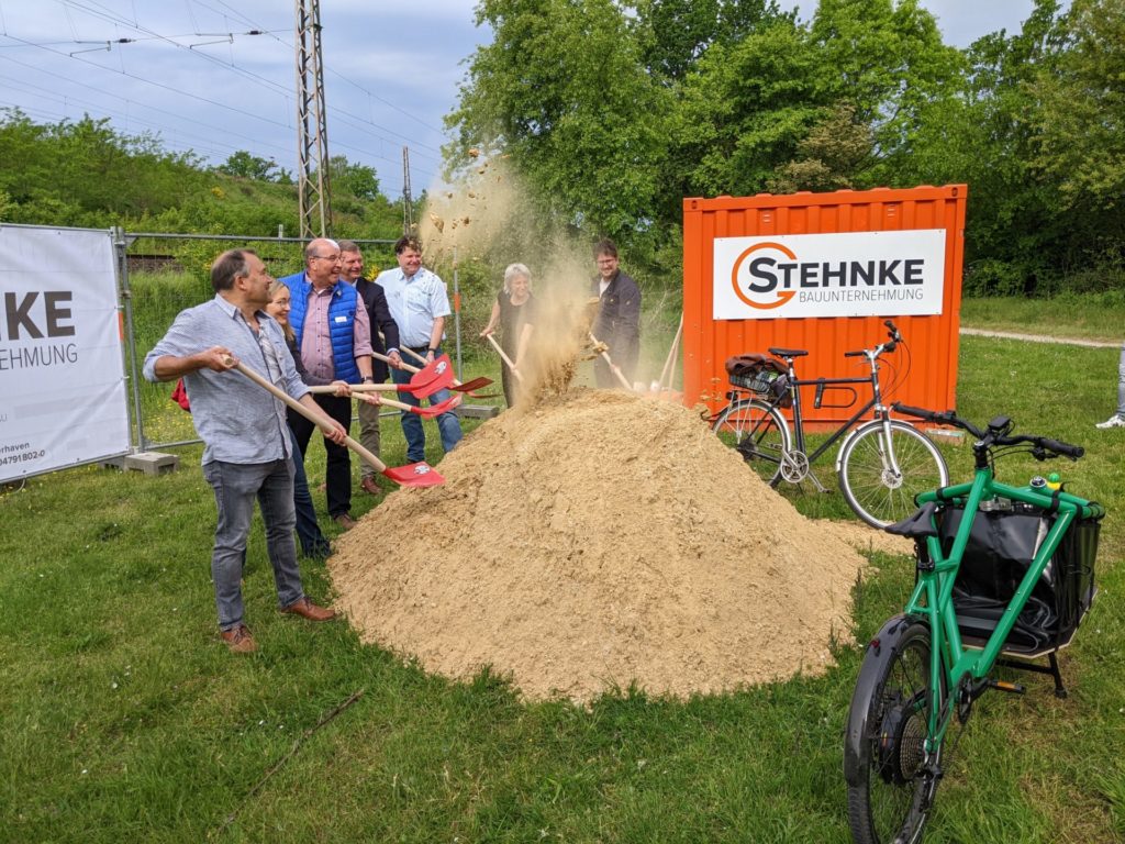 Menschen werfen beim symbolischen ersten Spatenstich Sand in die Luft.